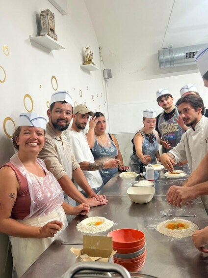 A group of people in a kitchen setting, wearing chef hats, preparing food with eggs and flour on a stainless steel table. 4