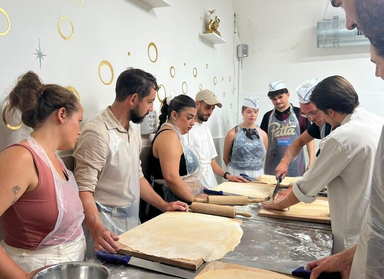 A group of people in a kitchen, rolling out dough on a large table. 2
