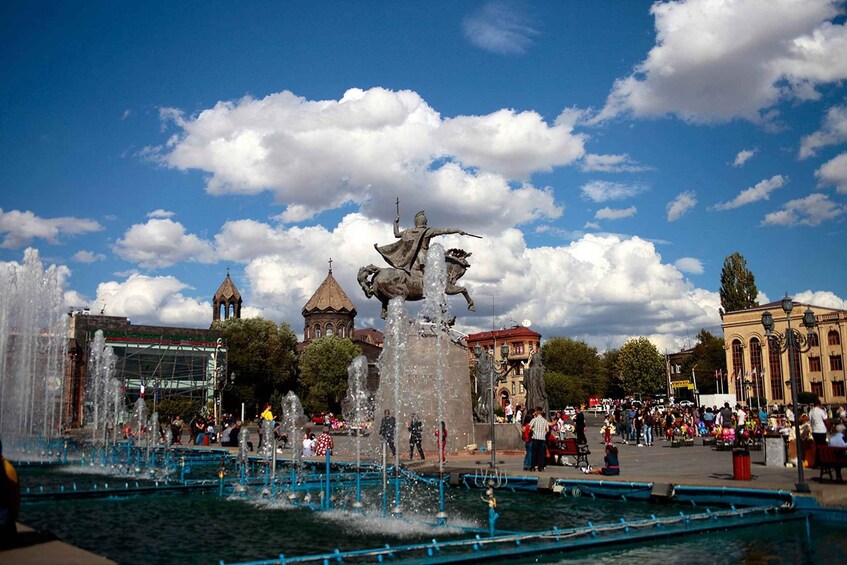 A fountain with a statue, a crowd of people, and historic buildings in the background. 3