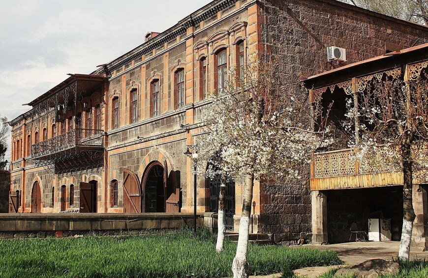 A historic building with ornate ironwork balconies and a large tree in the foreground. 2