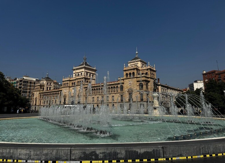 A historic building with two prominent towers and a fountain in front. 1