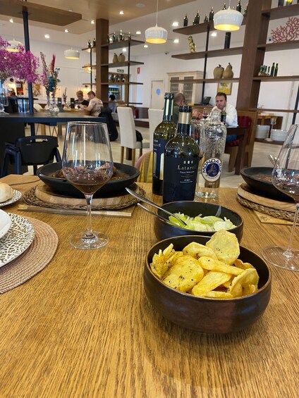 A restaurant interior with tables set for dining, wine bottles, and a bowl of chips. 1