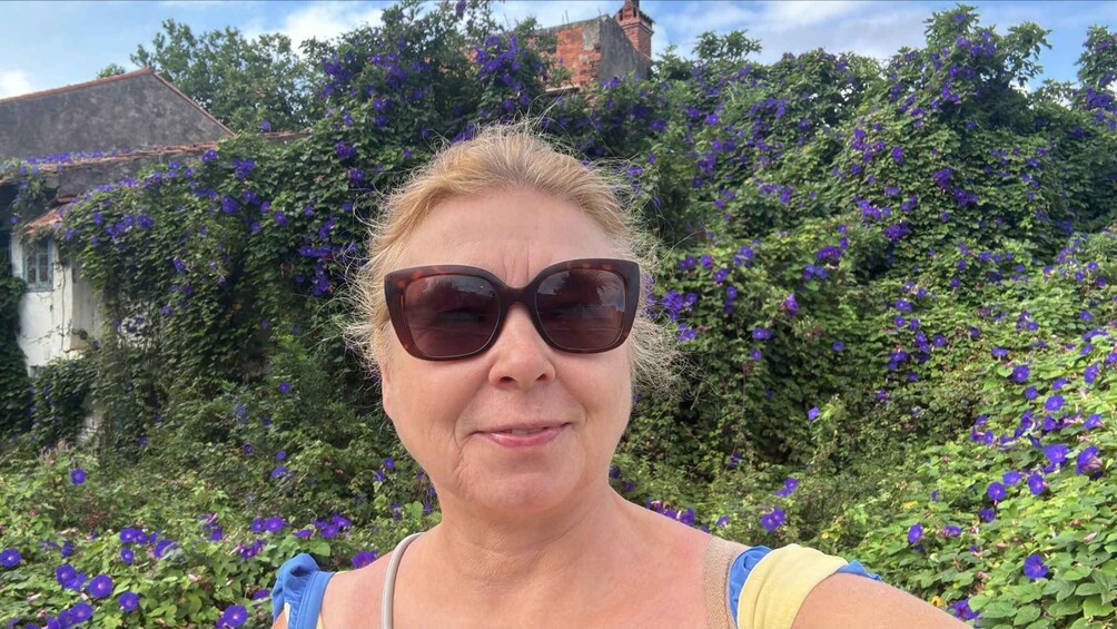 A person in a garden with purple flowers and a building in the background. 3