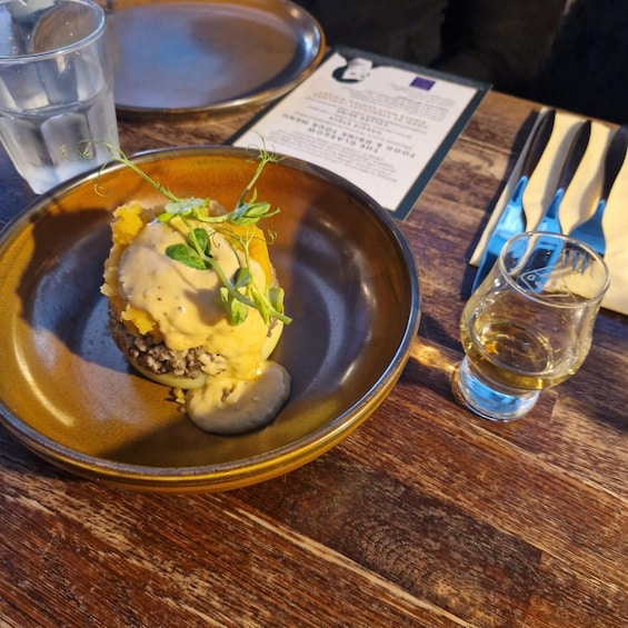 A dessert on a plate with a sprig of greenery, a glass of water, and a menu on a wooden table. 1