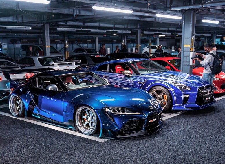 A blue sports car with a spoiler and a red sports car with a spoiler parked in a garage. 1