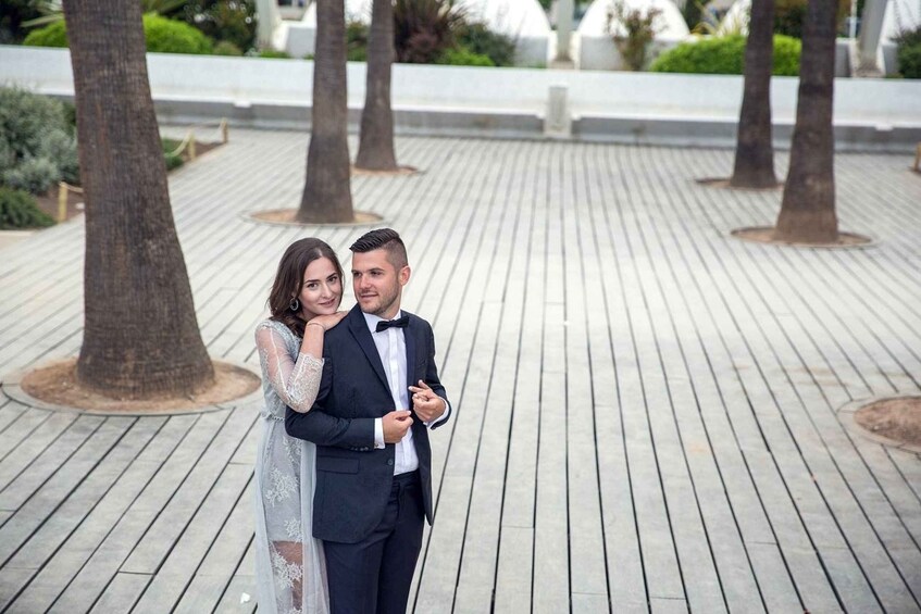 A couple standing on a wooden deck with trees and a white wall in the background. 2