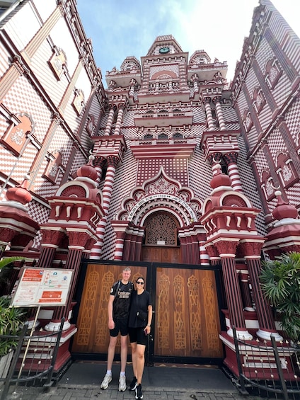 A man and a woman standing in front of a large, ornate gate with intricate designs and a clock. 2