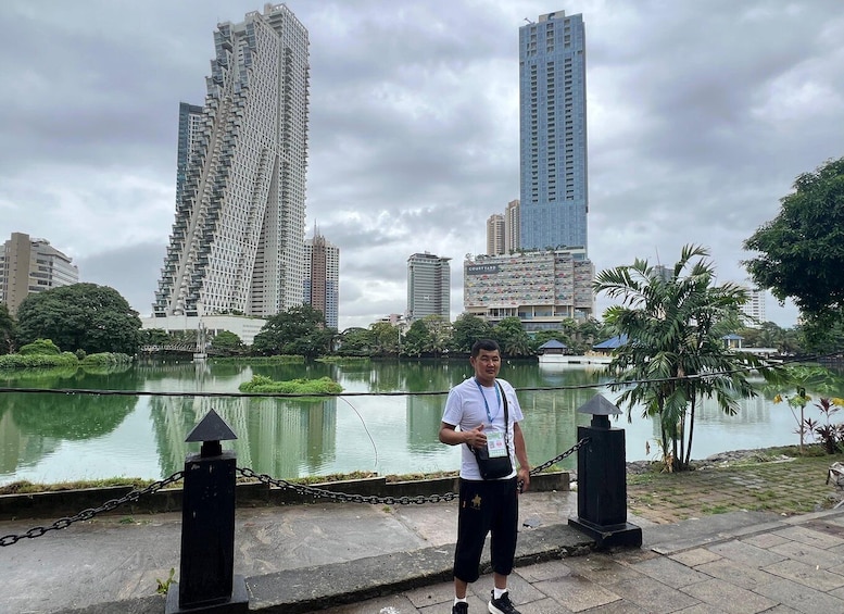 A man standing by a lake with tall buildings in the background. 5
