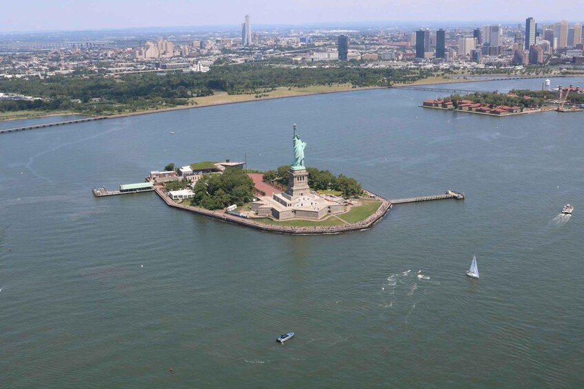 An aerial view of the Statue of Liberty on Liberty Island, surrounded by water with a city skyline in the background. 3
