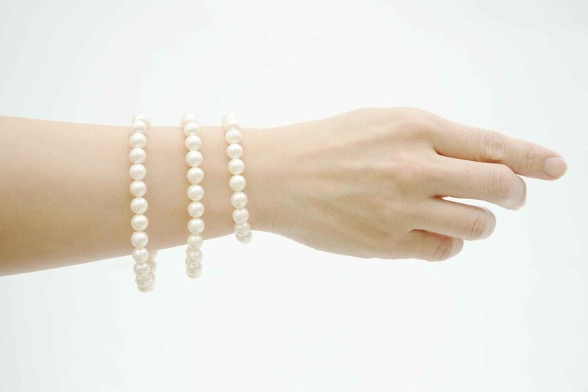 A hand with three pearl bracelets. 5
