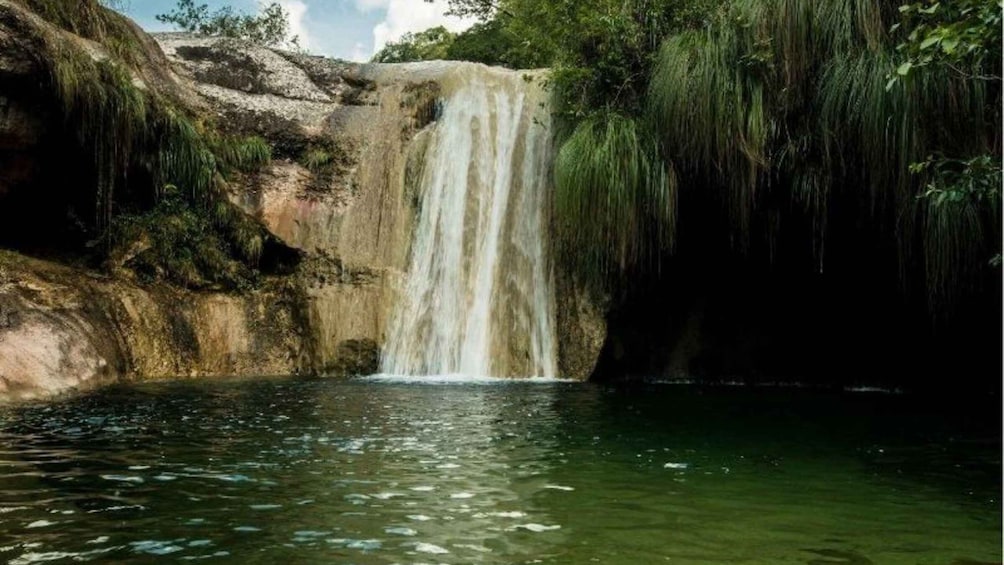 A waterfall cascading into a pool surrounded by rocky terrain and greenery. 1