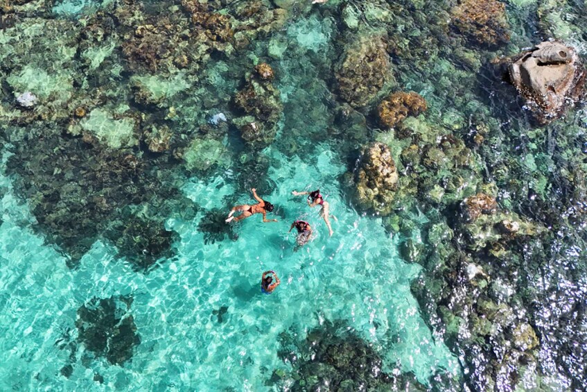A group of people swimming in clear turquoise water surrounded by rocky formations. 2