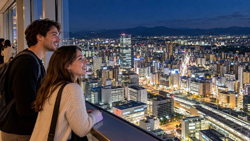 A cityscape at night with illuminated buildings and a mountain range in the background. 1