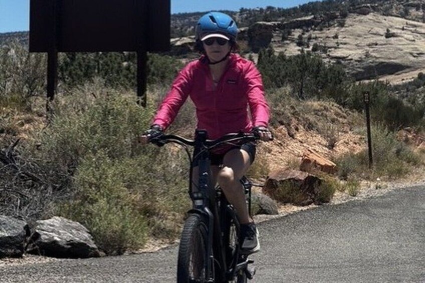 A person riding a bicycle on a road with a rocky hillside in the background. 5