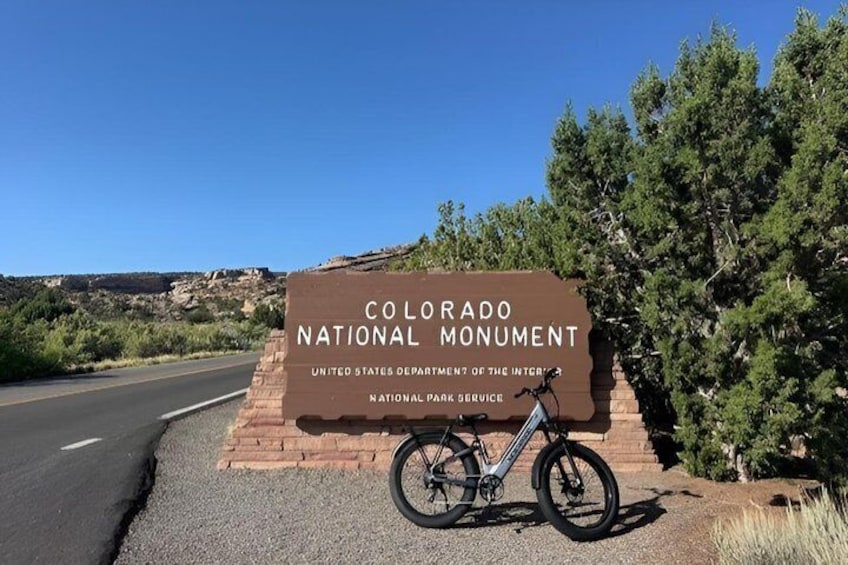 A sign for the Colorado National Monument with a bicycle parked in front. 1