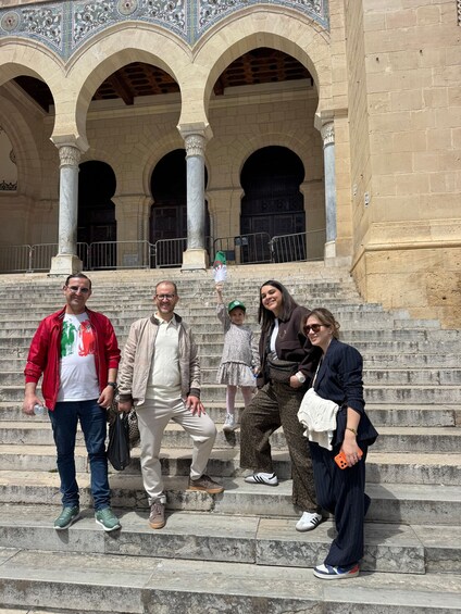 A group of people standing on stone steps in front of a building with arches and columns. 5