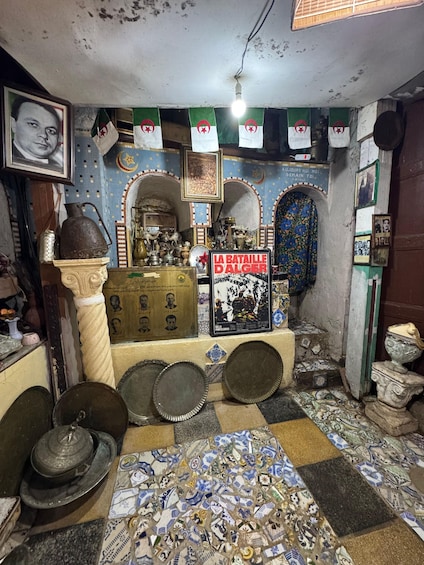 A room with a tiled floor, a shelf with various items, and a sign reading 'LA BATAILLE D'ALGER.' 1