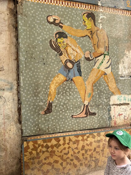 A mosaic of two figures in combat, a damaged wall, and a patterned floor. 4
