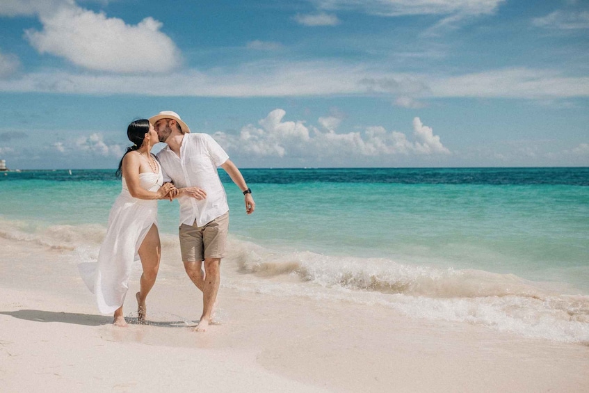 A couple walking on a beach with clear turquoise water and a boat in the distance. 1