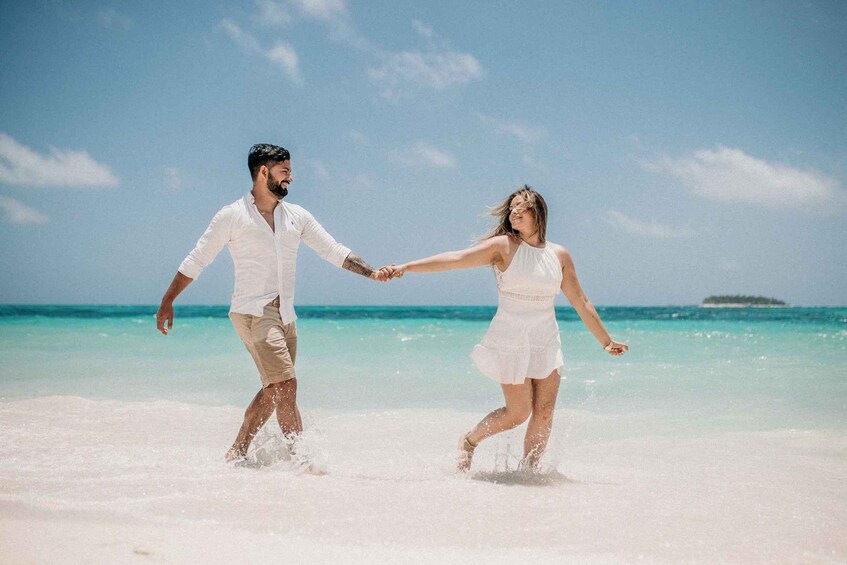 A couple holding hands on a beach with clear turquoise water and a small island in the distance. 3