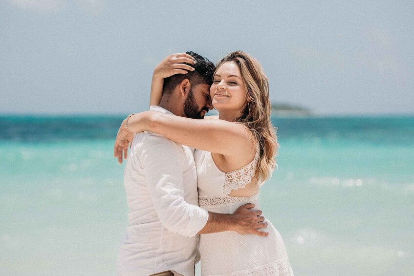 A couple embracing on a beach with clear turquoise water and a distant island. 5