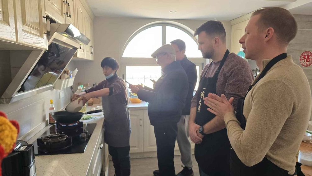 A group of people in a kitchen, some cooking and others observing. 4