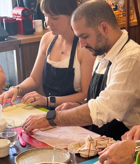 Two people working at a table with a cutting board, scissors, and a watch. 2