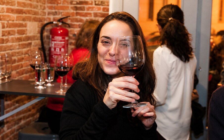 A person holding a wine glass, with a brick wall and a fire extinguisher in the background. 1
