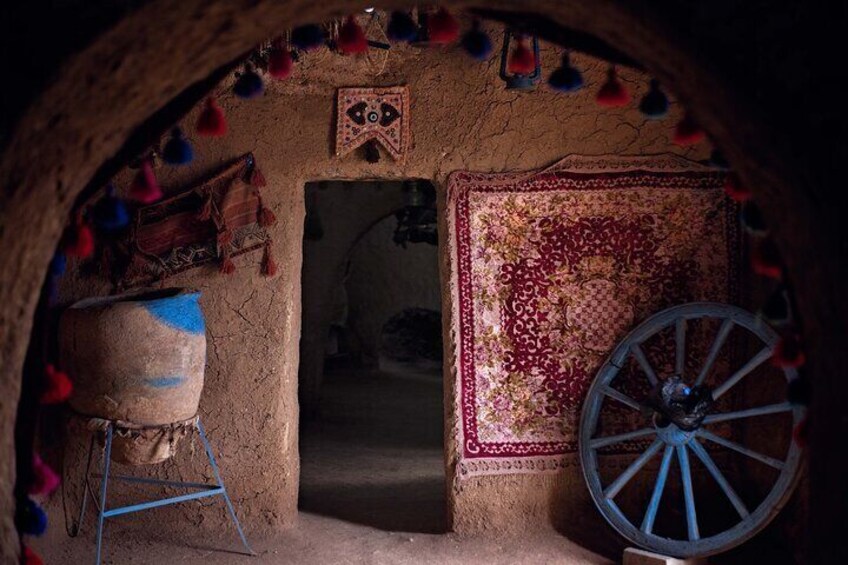 A rustic interior with a wheelbarrow, a patterned rug, and a traditional wall hanging. 3