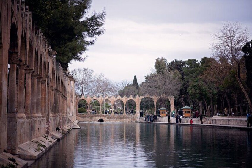 A historic stone bridge over a calm river, surrounded by trees and arches. 4