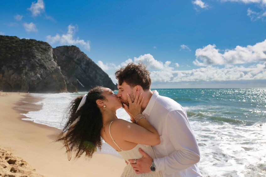 A couple embracing on a beach with ocean waves and a rocky cliff in the background. 5