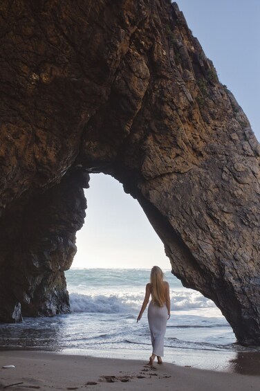 A woman walking towards a natural rock arch on a beach. 3