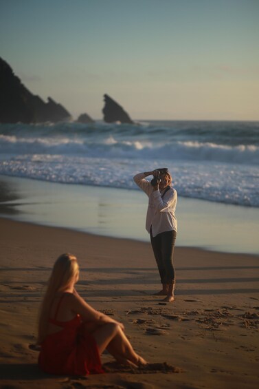 A beach with two people, one standing and taking a photo, and another sitting. 2