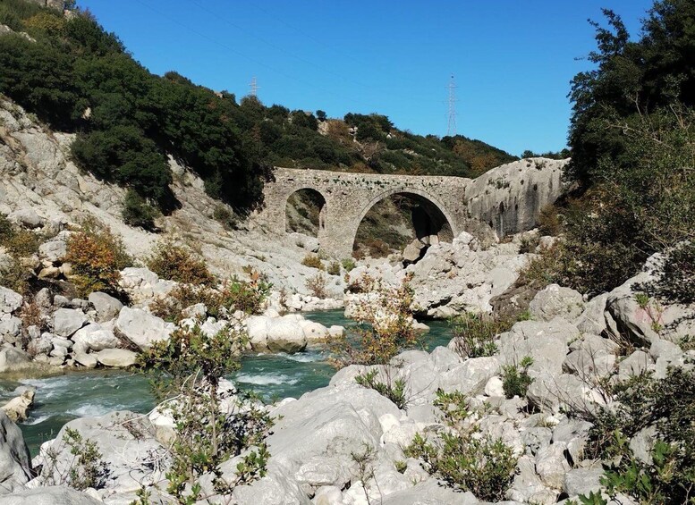 A stone bridge over a river with rocky terrain and greenery. 4