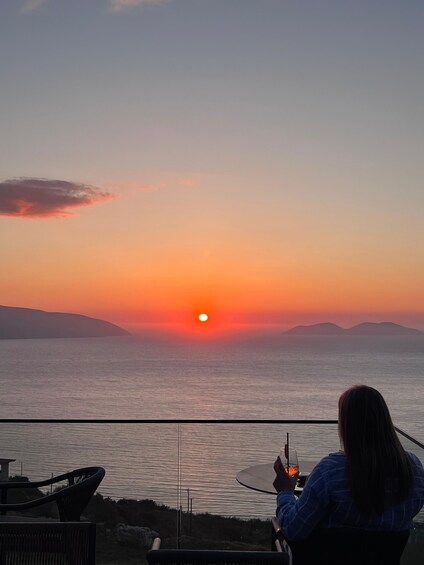 A sunset over the ocean with a person holding a drink. 1