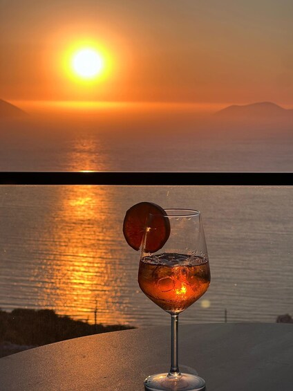 A sunset over a body of water with a glass of amber-colored drink and a slice of fruit on the table. 5