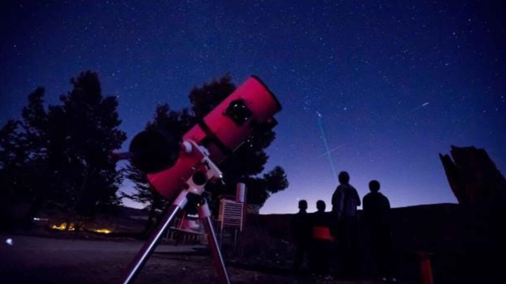 A telescope under a starry night sky with people observing. 4