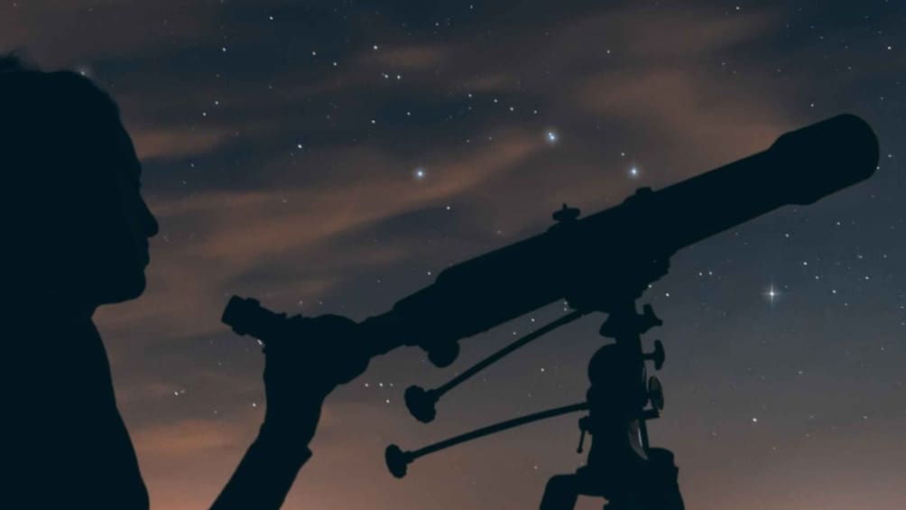A silhouette of a person using a telescope against a starry night sky. 3