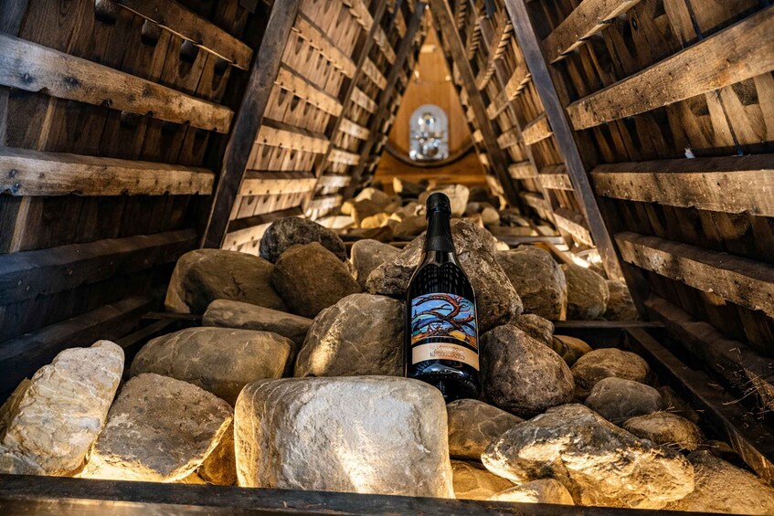 Een fles wijn in een houten wijnkelder, omringd door rotsen. 5