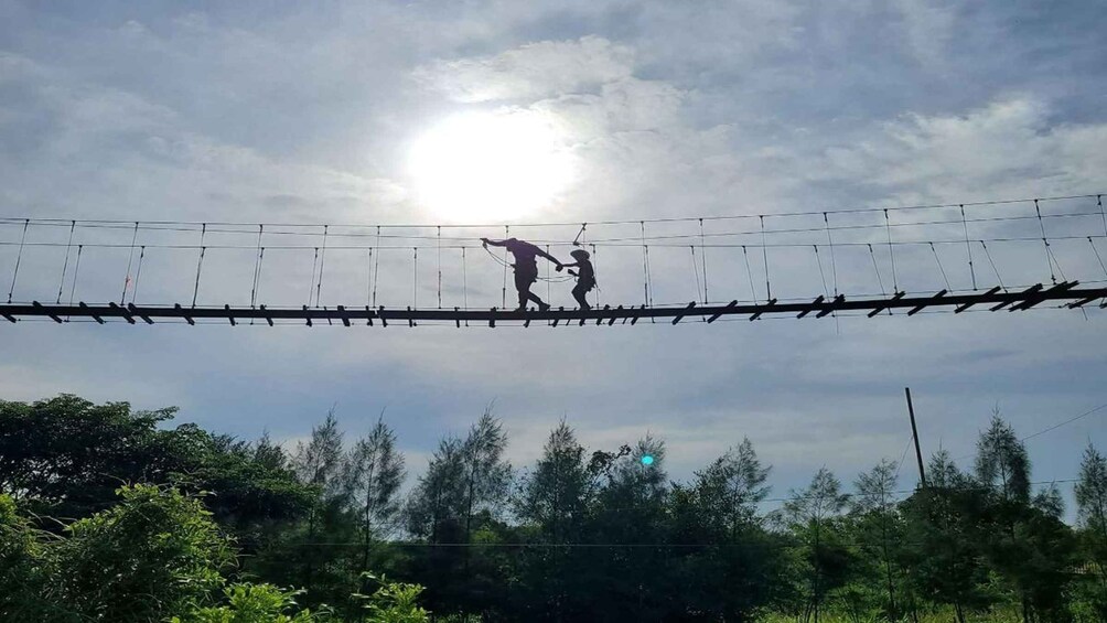Two people on a suspended bridge with a sun in the background. 2