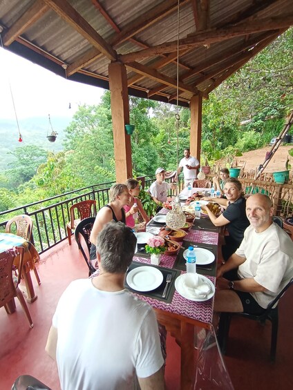 A group of people dining outdoors on a covered terrace with a scenic view of lush greenery and hills in the background. 3
