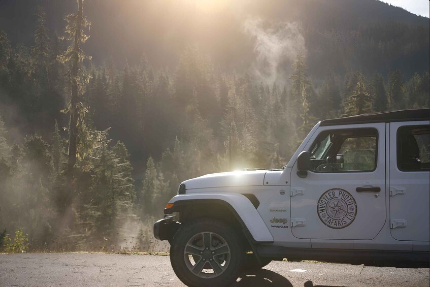 A white SUV with 'Wheeler Photo Safaris Ltd' on the side parked on a road with a forested mountain background. 3