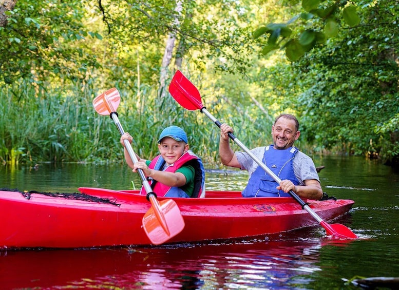 Two people kayaking in a red canoe on a river surrounded by lush greenery. 1