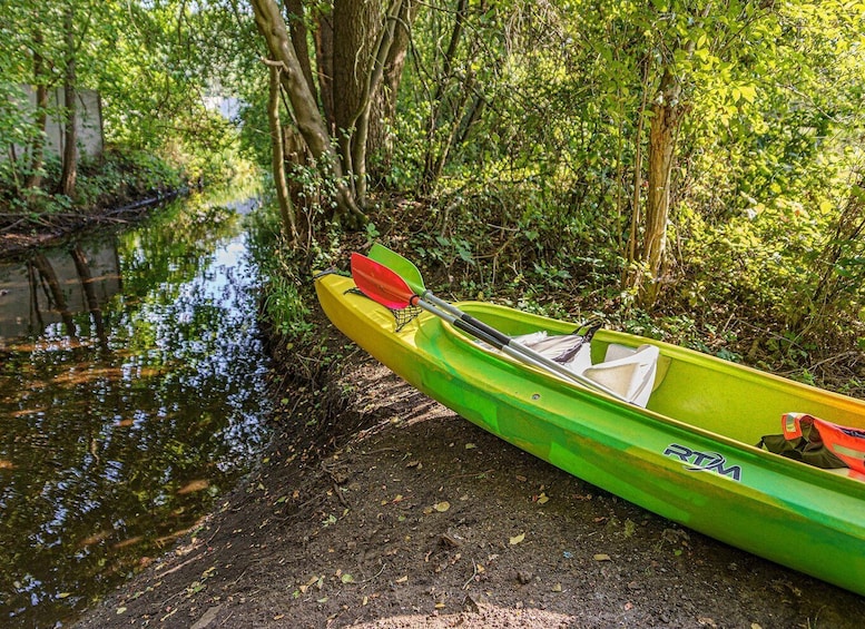 A green kayak with a paddle resting on it, docked at the edge of a calm river surrounded by dense greenery. 4