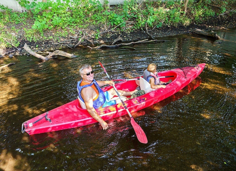 Two people kayaking on a calm river surrounded by greenery. 2