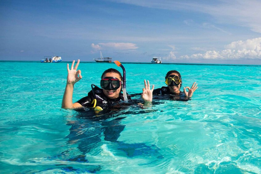 Two people snorkeling in clear turquoise water with boats in the background. 1