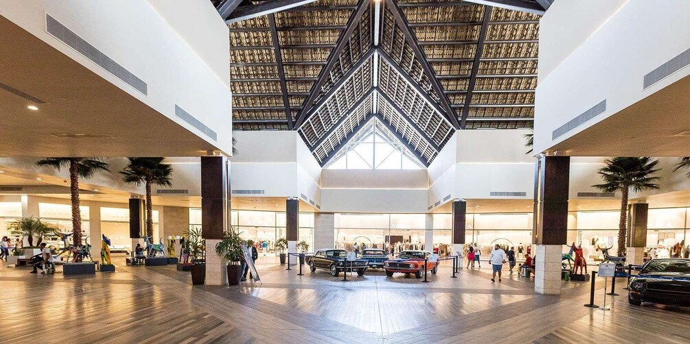 A spacious indoor atrium with a high ceiling, wooden flooring, and a central display of vintage cars. 2