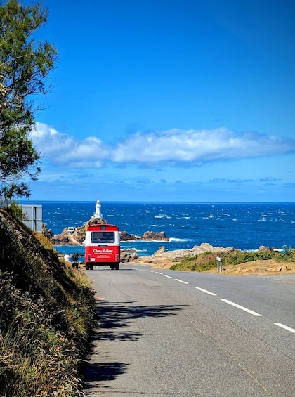 A red bus on a coastal road with ocean and rocky cliffs in the background. 1