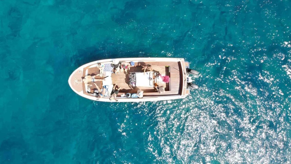 Luchtbeeld van een boot met mensen op het dek, omringd door helder turquoise water. 1