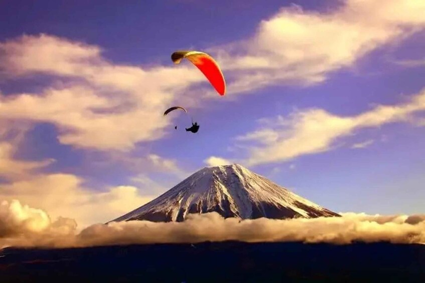 Et bjerg med en rød faldskærm og en sort paraglider på himlen. 2